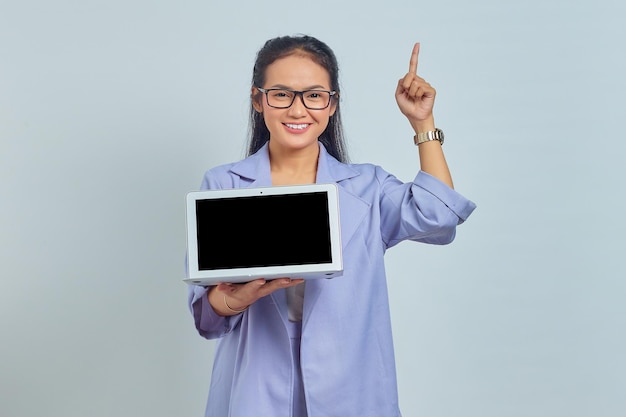 Portrait of smiling young Asian woman showing laptop and pointing finger up isolated on white background