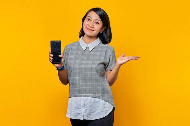 Portrait of smiling young Asian woman showing  smartphone blank screen  and pointing to empty space with palms