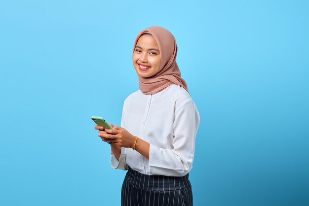 Portrait of smiling young Asian woman using mobile phone and looking at camera