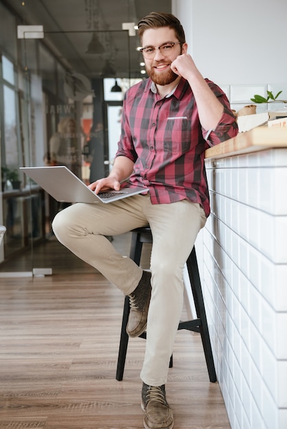 Portrait of smiling young bearded man sitting with laptop