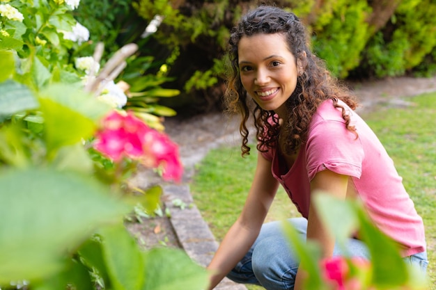 Portrait of smiling young biracial woman with curly hair gardening in backyard