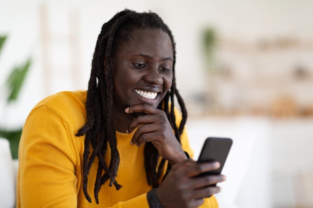 Ritratto di giovane ragazzo nero sorridente utilizzando smartphone a casa