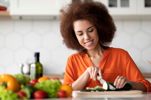 Portrait of smiling young black woman cooking vegetable salad in kitchen