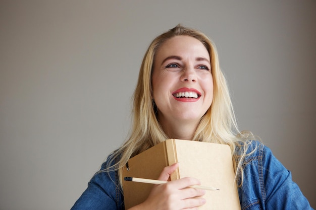 Photo portrait of smiling young blond female student holding books and pencil