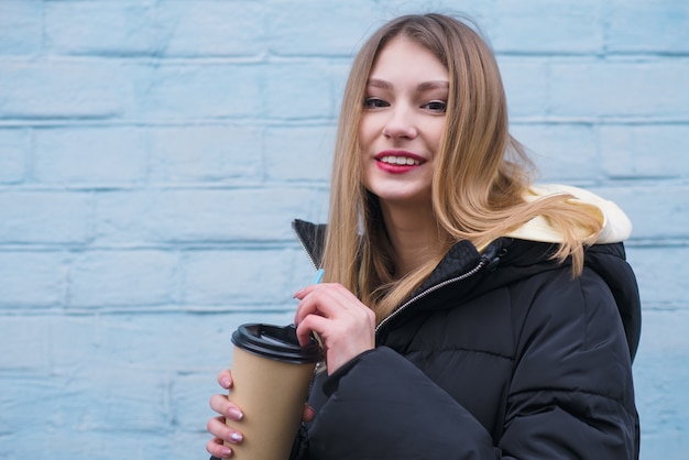 Portrait of a smiling young blond girl with a cup of warm coffee in her hands