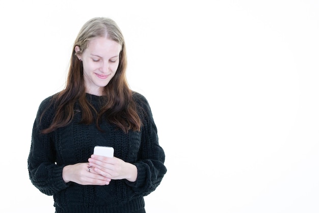 白い背景に分離された携帯電話のテキスト メッセージの電話を使用して笑顔の若い金髪白人女性の肖像画