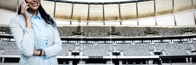 Portrait of smiling young businesswoman talking on cellphone\
against rugby goal post in a stadium front view of rugby goal post\
in a empty stadium