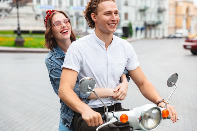 街の通りで一緒にバイクに乗って笑顔の若いカップルの肖像画