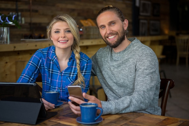 Portrait of smiling young couple with coffee and technologies in cafe