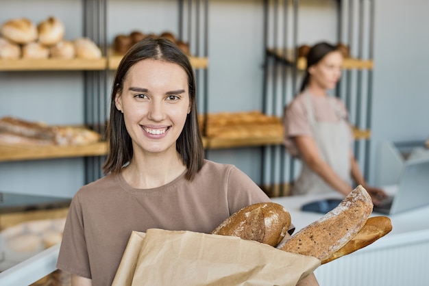 Ritratto di giovane cliente sorridente che tiene la pagnotta appena sfornata in aperbag contro lo stallo