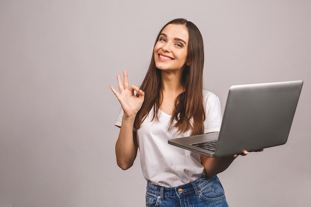 Foto ritratto di una ragazza sorridente che tiene il computer portatile e che mostra il gesto giusto