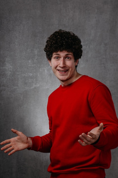 Foto ritratto di un giovane uomo bello e sorridente in maglione rosso che guarda la telecamera su uno studio grigio isolato