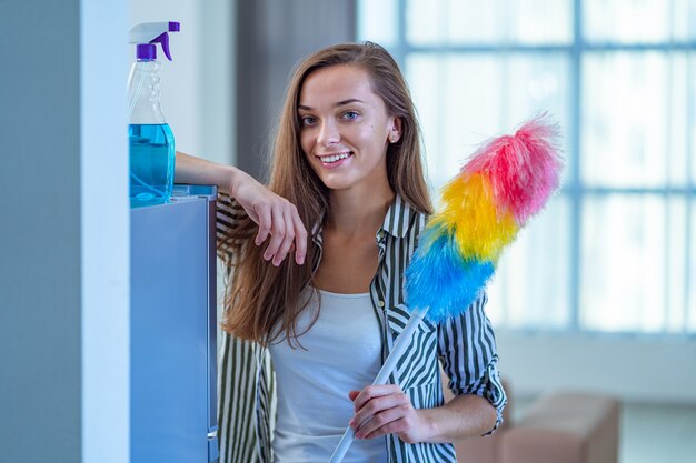 Portrait of smiling young happy joyful cleaning woman with a dust brush and spray bottle during house cleaning. Household chores and housework