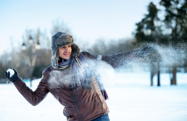 Portrait of a smiling young man in an ear flap hat with a snowball in his hand