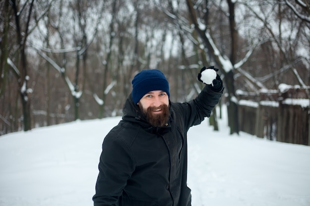 Foto ritratto di un giovane sorridente con un cappello e una palla di neve in mano