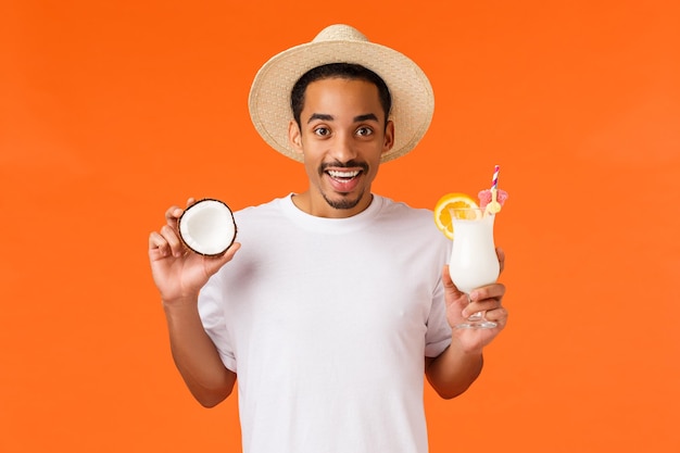 Photo portrait of smiling young man holding hat against orange background