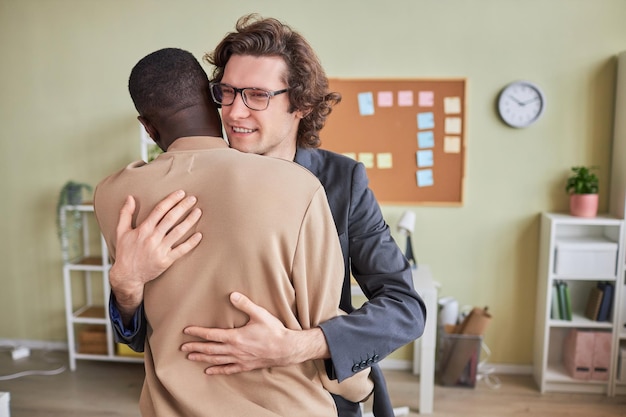 Photo portrait of smiling young man hugging colleague in office as friendly greeting copy space