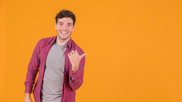 Photo portrait of a smiling young man showing thumb up sign against an orange backdrop