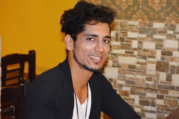 Photo portrait of smiling young man sitting against brick wall