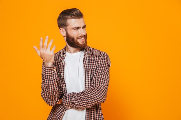 Portrait of a smiling young man wearing casual clothes standing isolated over yellow wall, looking away at copy space