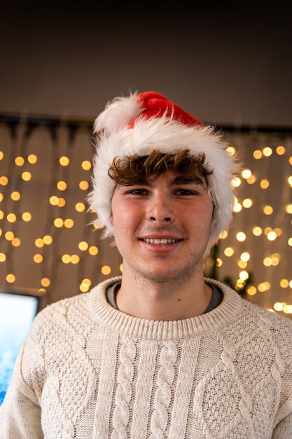 Foto ritratto di un giovane sorridente che indossa un cappello rosso davanti a un muro di luci di natale