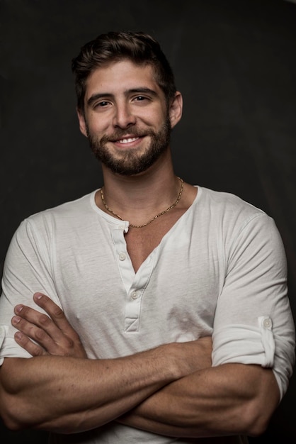 portrait of smiling young man with arms crossed standing against black background