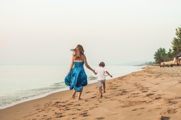 ビーチで走っている小さな子供と笑顔の若い母親の肖像画。