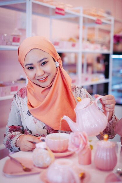 Portrait of a smiling young muslimah woman wearing hijab holding a teapot