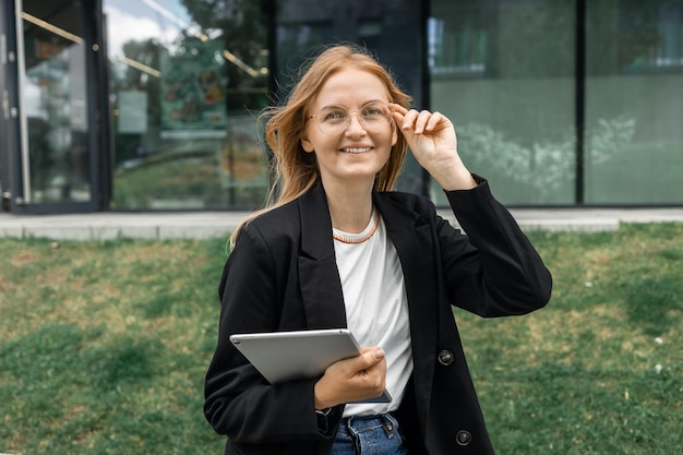 Portrait of smiling young pretty business woman at outdoors holding a tablet with happy expression h