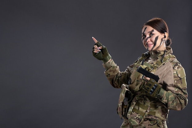 Portrait of smiling young soldier in camouflage with gun on dark wall
