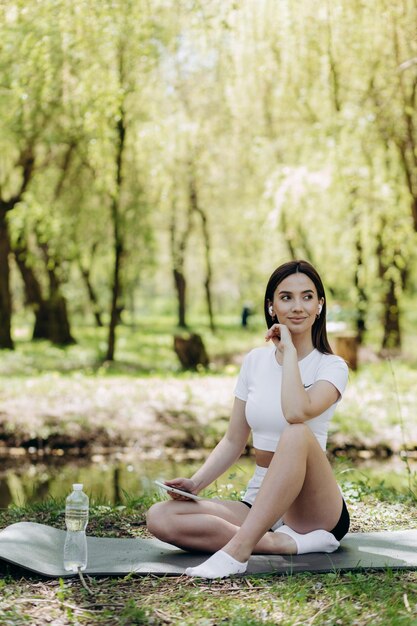 Photo portrait of a smiling young sporty woman using mobile phone in the park before doing exercise