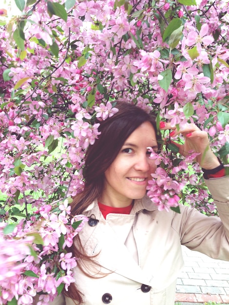 Foto ritratto di una giovane donna sorridente in mezzo a fiori rosa durante la primavera