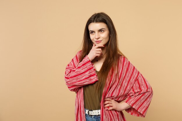 Portrait of smiling young woman in casual clothes looking aside, put hand prop up on chin isolated on pastel beige background in studio. People sincere emotions, lifestyle concept. Mock up copy space.