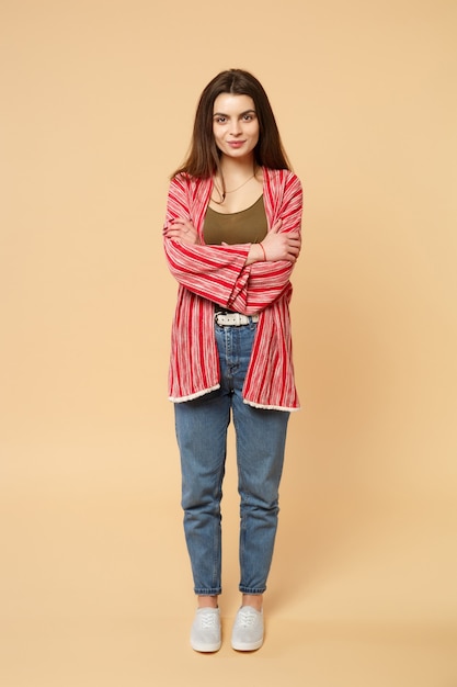 Portrait of smiling young woman in casual clothes looking camera, holding hands crossed isolated on pastel beige background in studio. People sincere emotions, lifestyle concept. Mock up copy space.