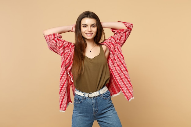 Portrait of smiling young woman in casual clothes putting hands behind head looking camera isolated on pastel beige background in studio. People sincere emotions lifestyle concept. Mock up copy space.