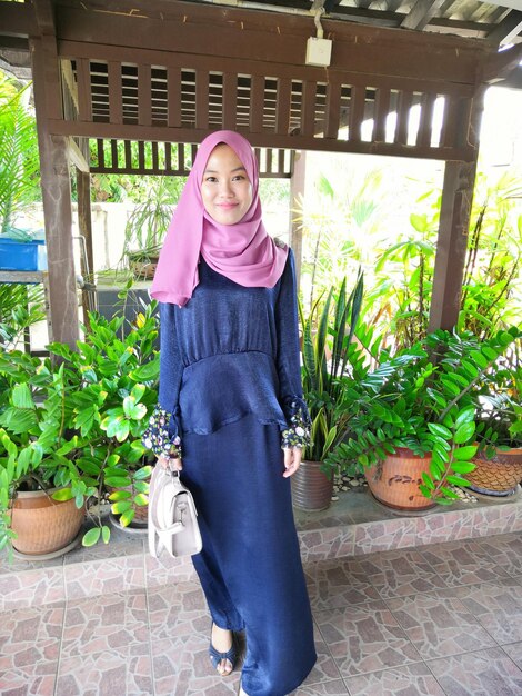 Portrait of smiling young woman in headscarf standing against plants