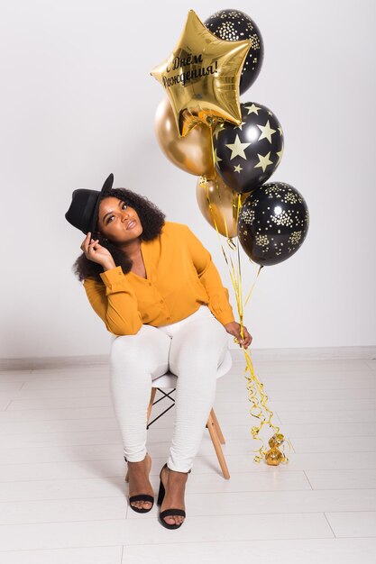 Photo portrait of smiling young woman holding balloons against wall