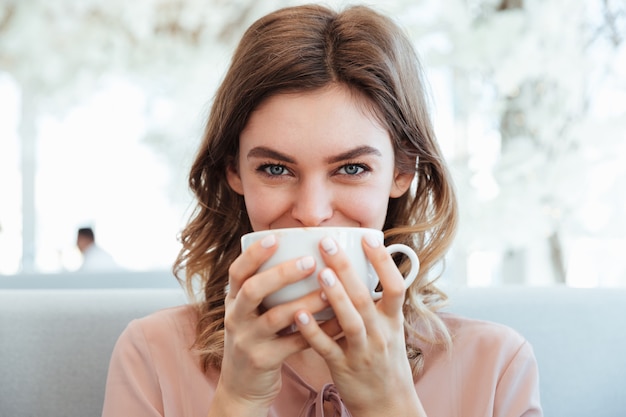 一杯のコーヒーを保持している笑顔の若い女性の肖像画