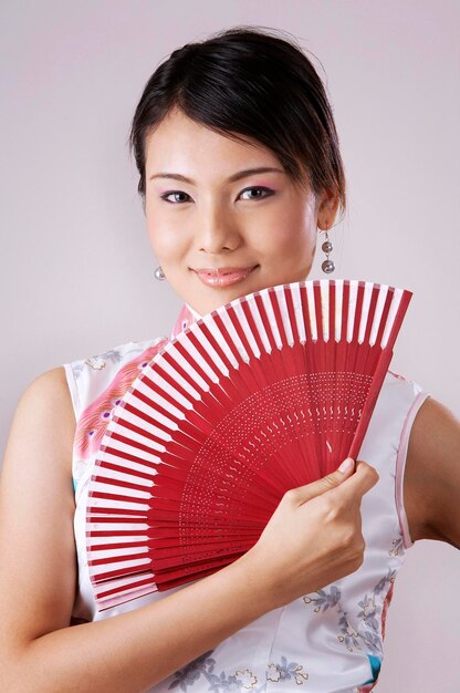 Photo portrait of smiling young woman holding hand fan against gray background