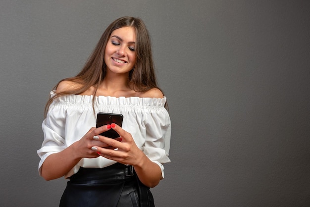 壁に立ってスマートフォンを握っている笑顔の若い女性の肖像画