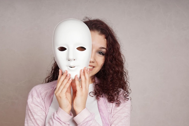 Photo portrait of smiling young woman behind mask against gray background