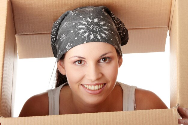 Foto ritratto di una giovane donna sorridente che sbircia attraverso una scatola aperta su uno sfondo bianco