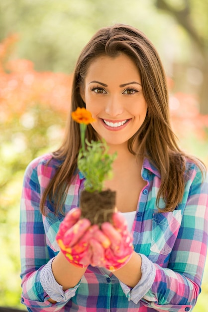 Foto ritratto di una giovane donna sorridente che pianta fiori in giardino. guardando la fotocamera.