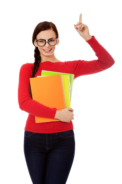 Photo portrait of smiling young woman pointing while holding books against white background