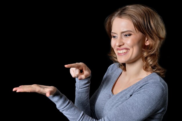 Portrait of smiling young woman showing something  isolated on black  background