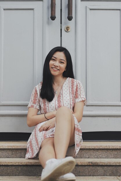 Photo portrait of smiling young woman sitting against door