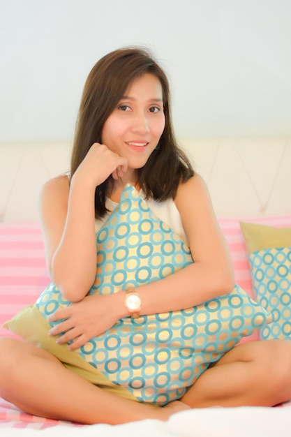 Photo portrait of a smiling young woman sitting on bed at home