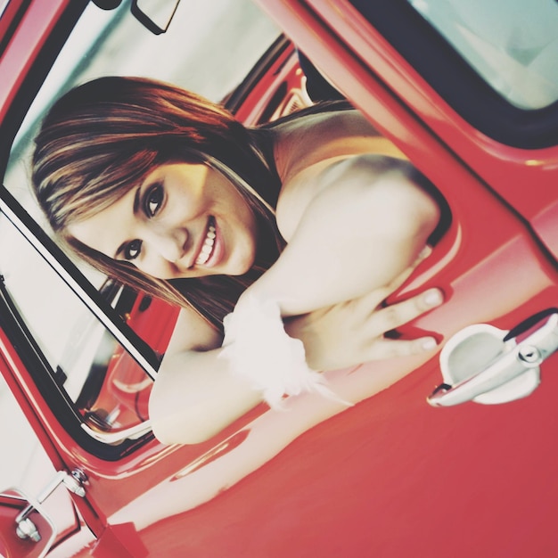 Photo portrait of smiling young woman sitting in red car