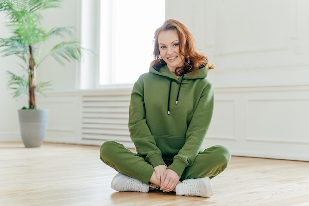 Photo portrait of a smiling young woman sitting on wooden floor