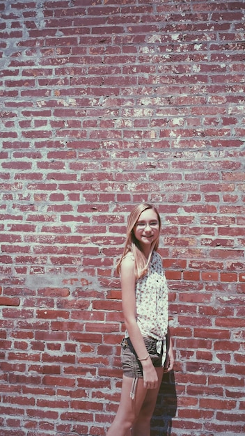 Portrait of smiling young woman standing against brick wall